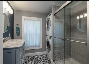 Een moderne badkamer met een ingebouwde wasmachine, een douchecabine van glas en een vloer met een patroon.