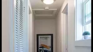 A narrow hallway with wooden flooring, white walls, and a ceiling light. A framed picture hangs on the wall. - *New* The Foundry Getaway 2BR / 1 BR (Saranac Lake)