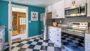 A kitchen with white cabinets, a black and white checkered floor, a wooden door, and a wall-mounted oven. - *New* The Foundry Getaway 2BR / 1 BR (Saranac Lake)