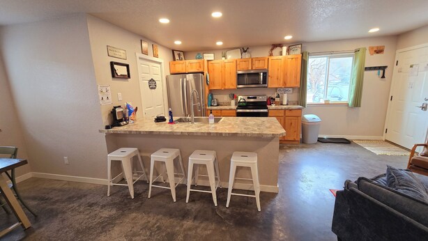 A compact kitchen with wooden cabinets, a stainless steel refrigerator, a microwave, and a sink. There are four white stools at the kitchen island.