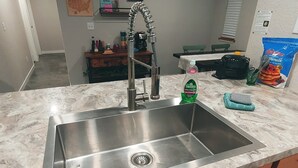A kitchen with a stainless steel sink, wooden cabinets, and a marble countertop.