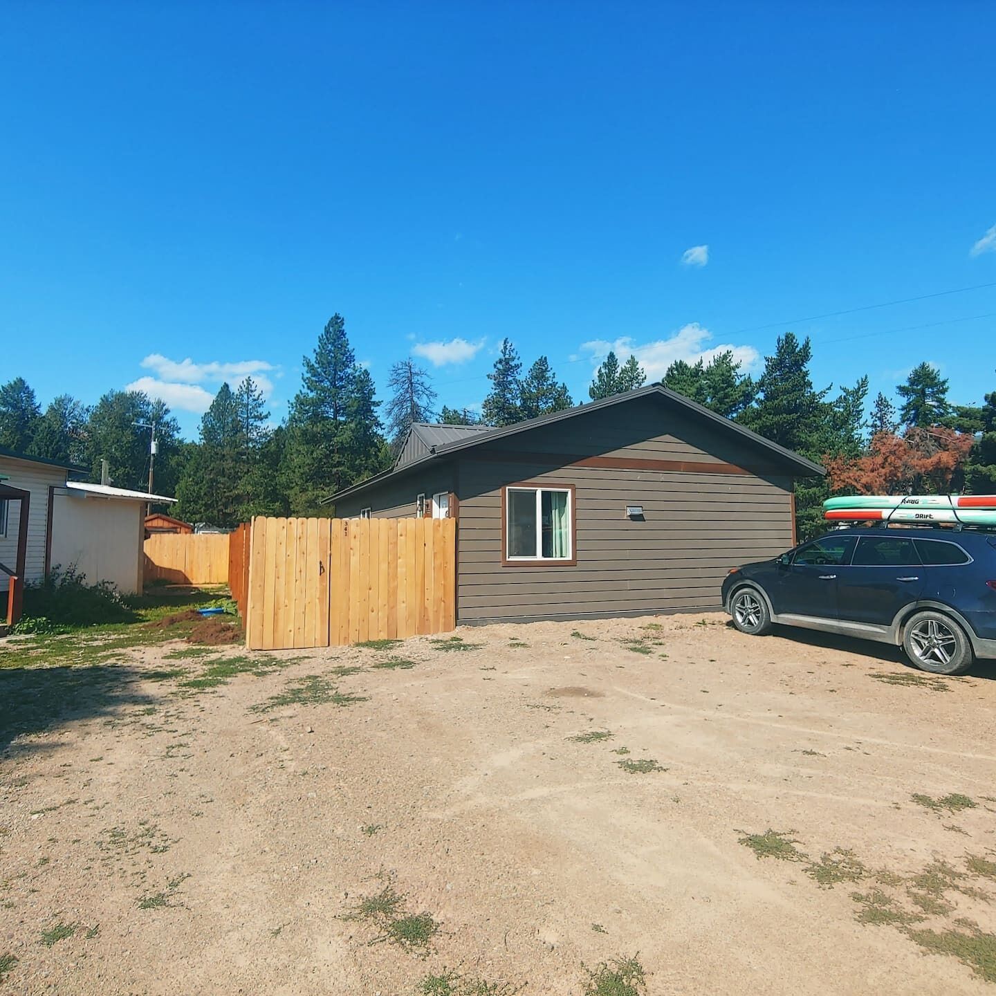 A single-story house with a fenced yard, a parked SUV, and a clear blue sky.