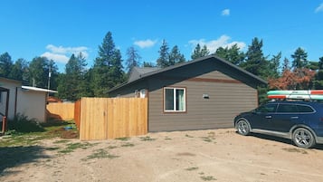 A single-story house with a fenced yard, a parked SUV, and a clear blue sky.