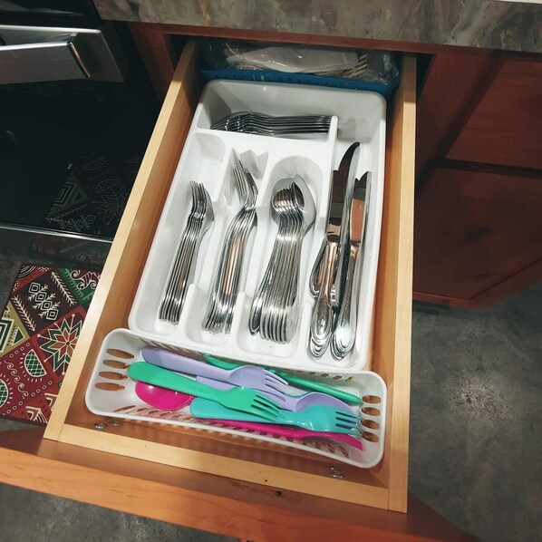 A drawer containing neatly organized silverware and colorful plastic utensils.