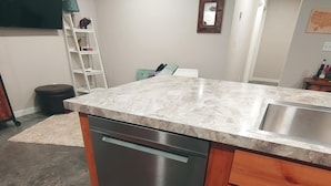 A kitchen with a dishwasher, wooden cabinets, a marble countertop, and a stainless steel sink.