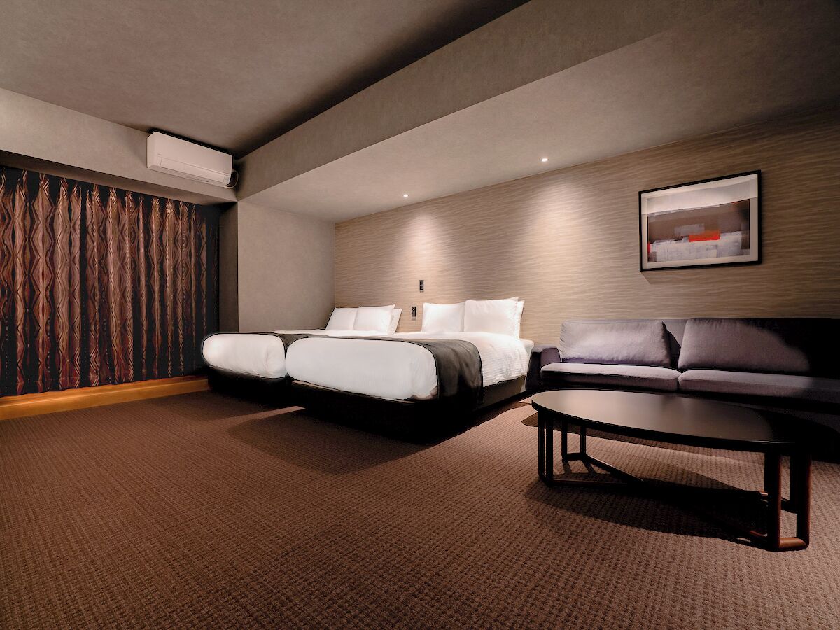 A hotel room with a bed, a sofa, a coffee table, and a wall-mounted air conditioner.