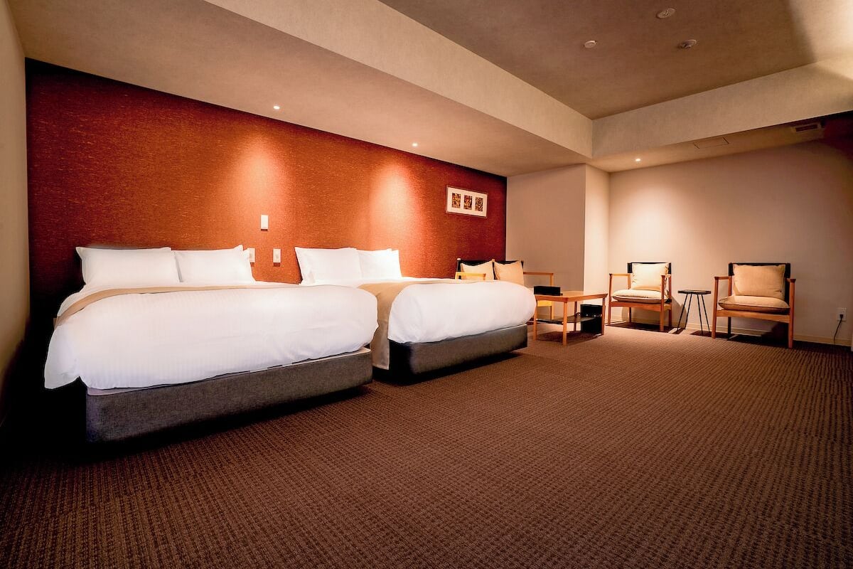 Habitación de hotel con dos camas, una mesita, dos sillas y piso alfombrado.