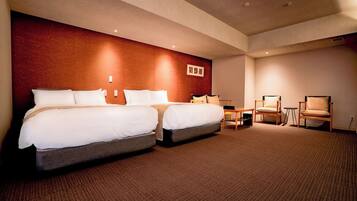 A hotel room with two beds, a small table, two chairs, and a carpeted floor.