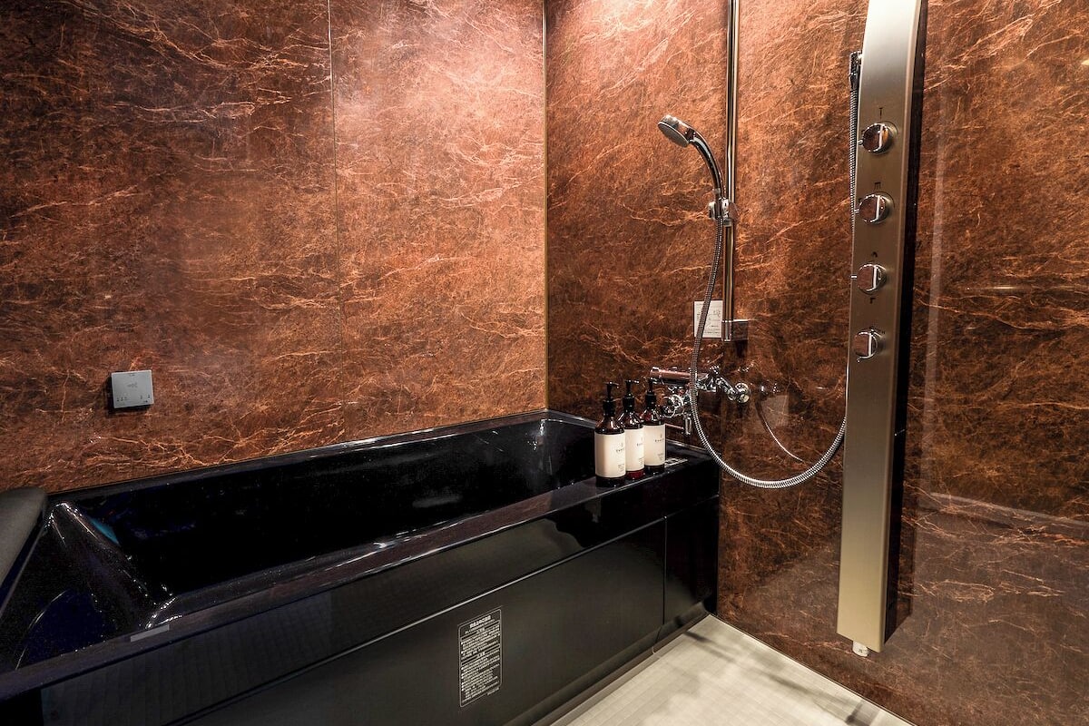 Un baño moderno con una bañera negra, ducha con cabezal de ducha de mano y paredes de mármol.