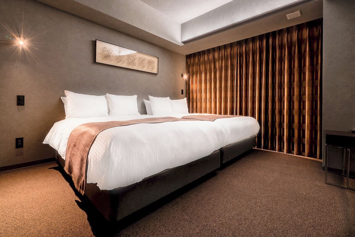 Una habitación de hotel moderna con una cama grande, una obra de arte enmarcada en la pared y una ventana con cortinas.
