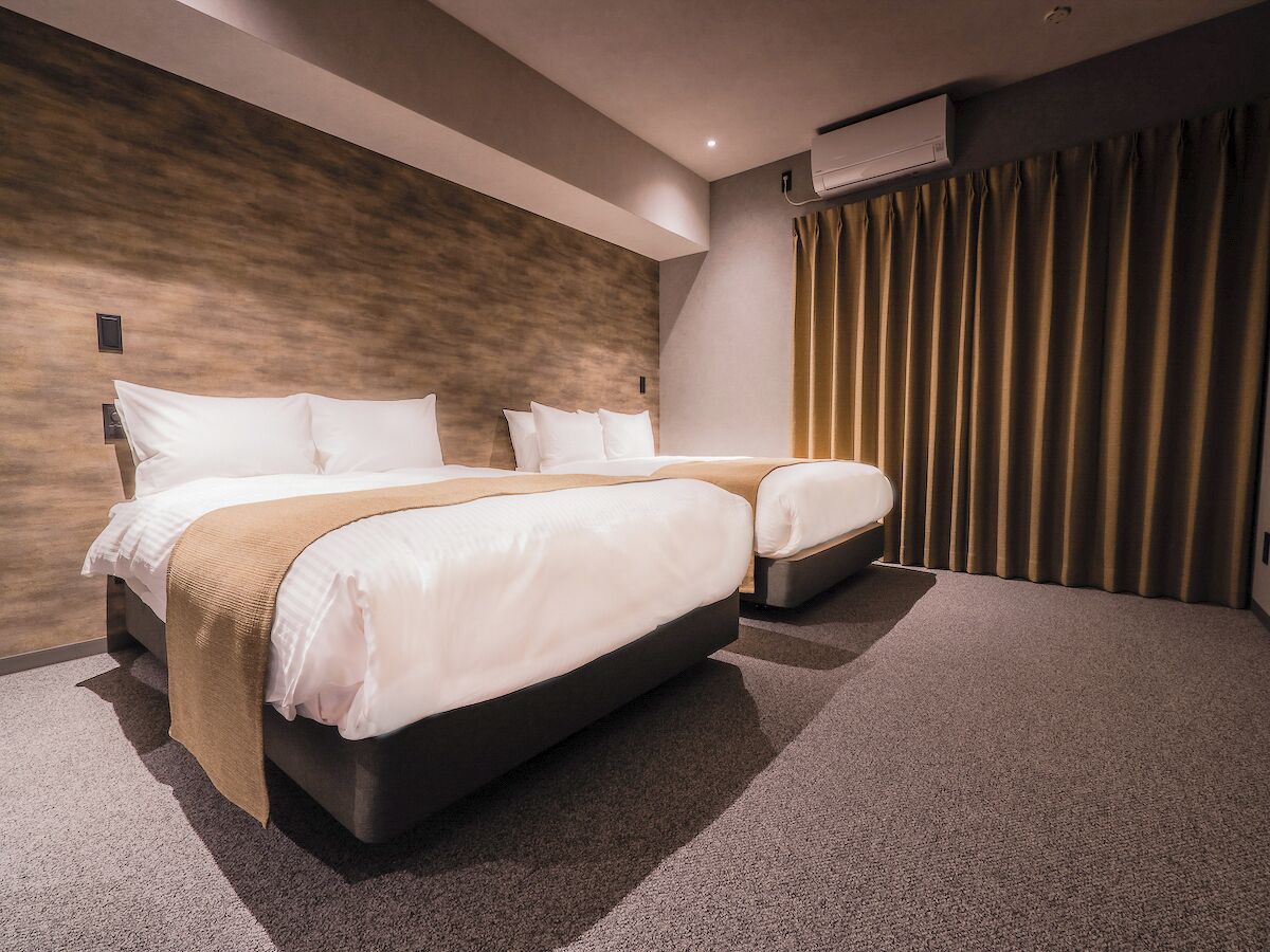 A modern hotel room with a large bed, a smaller bed, and a separate seating area.
