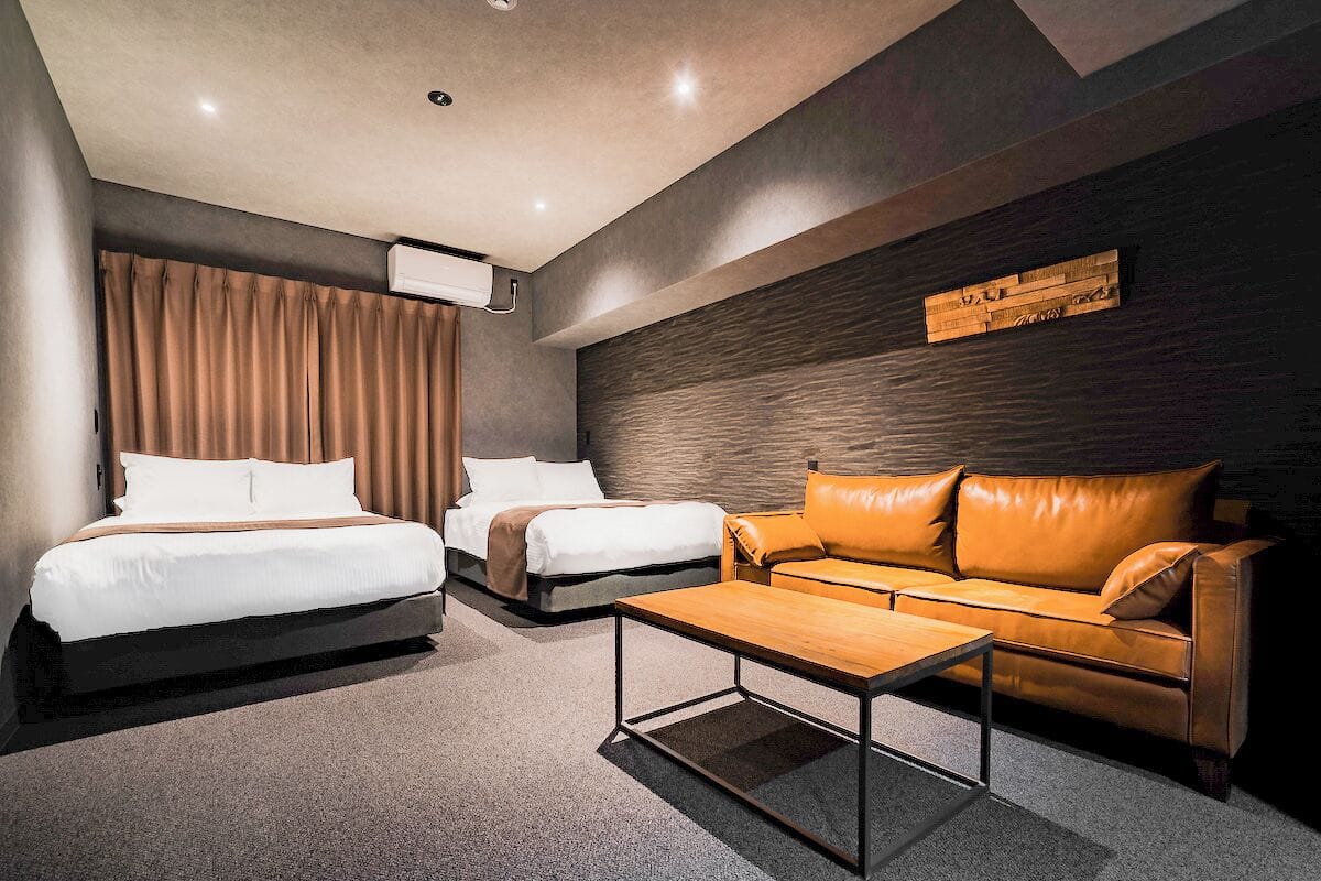 Una habitación de hotel con dos camas, un sofá, una mesa de centro y un aire acondicionado instalado en la pared.