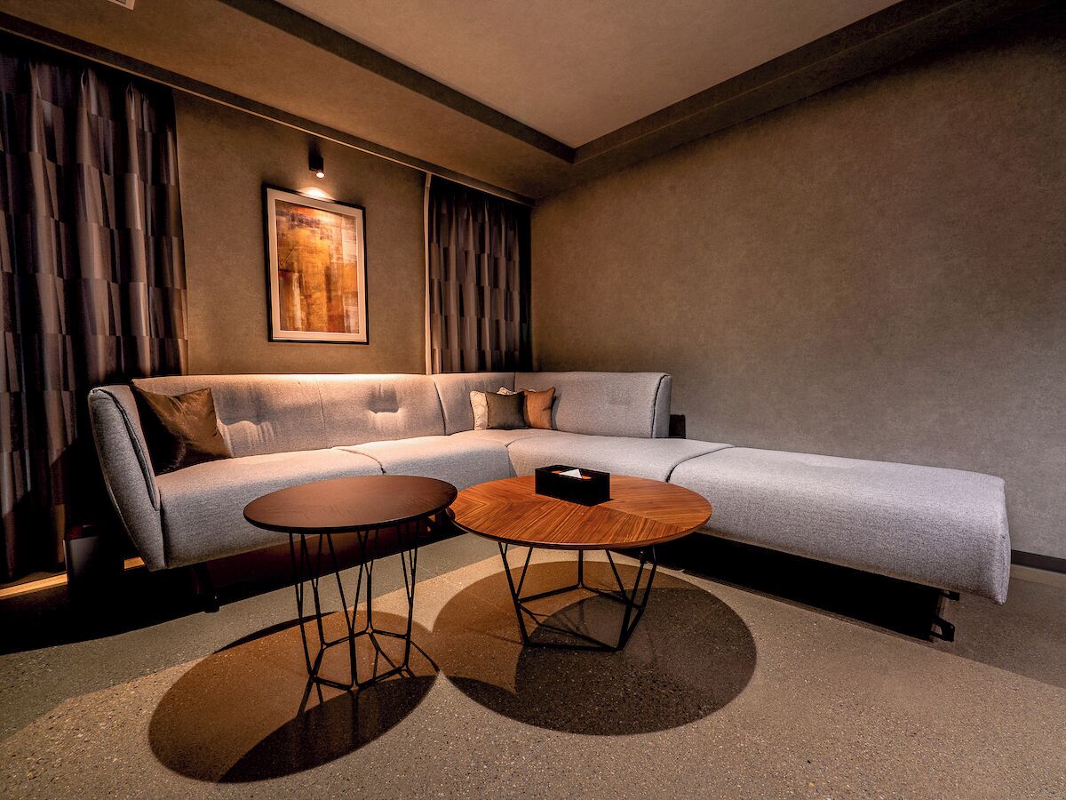 Ein modernes Wohnzimmer mit einem grauen Ecksofa, zwei runden Couchtischen und einem großen abstrakten Gemälde an der Wand.