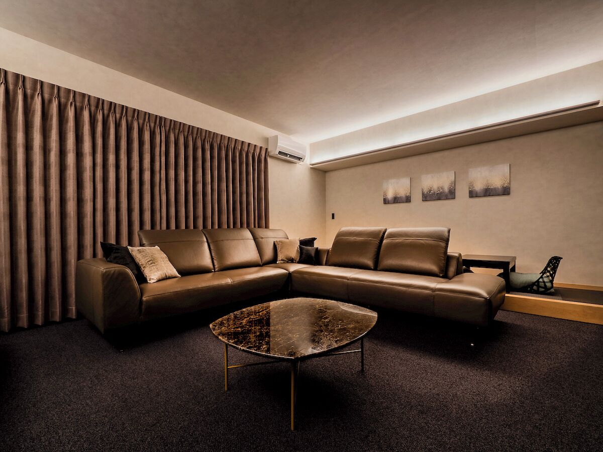 Un salon moderne avec un canapé d’angle, une table basse ronde et une grande fenêtre agrémentée de rideaux.