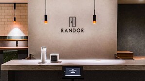Een modern receptiebalie met een minimalistisch ontwerp, met een logo, een digitaal scherm en een klein zitgedeelte.
