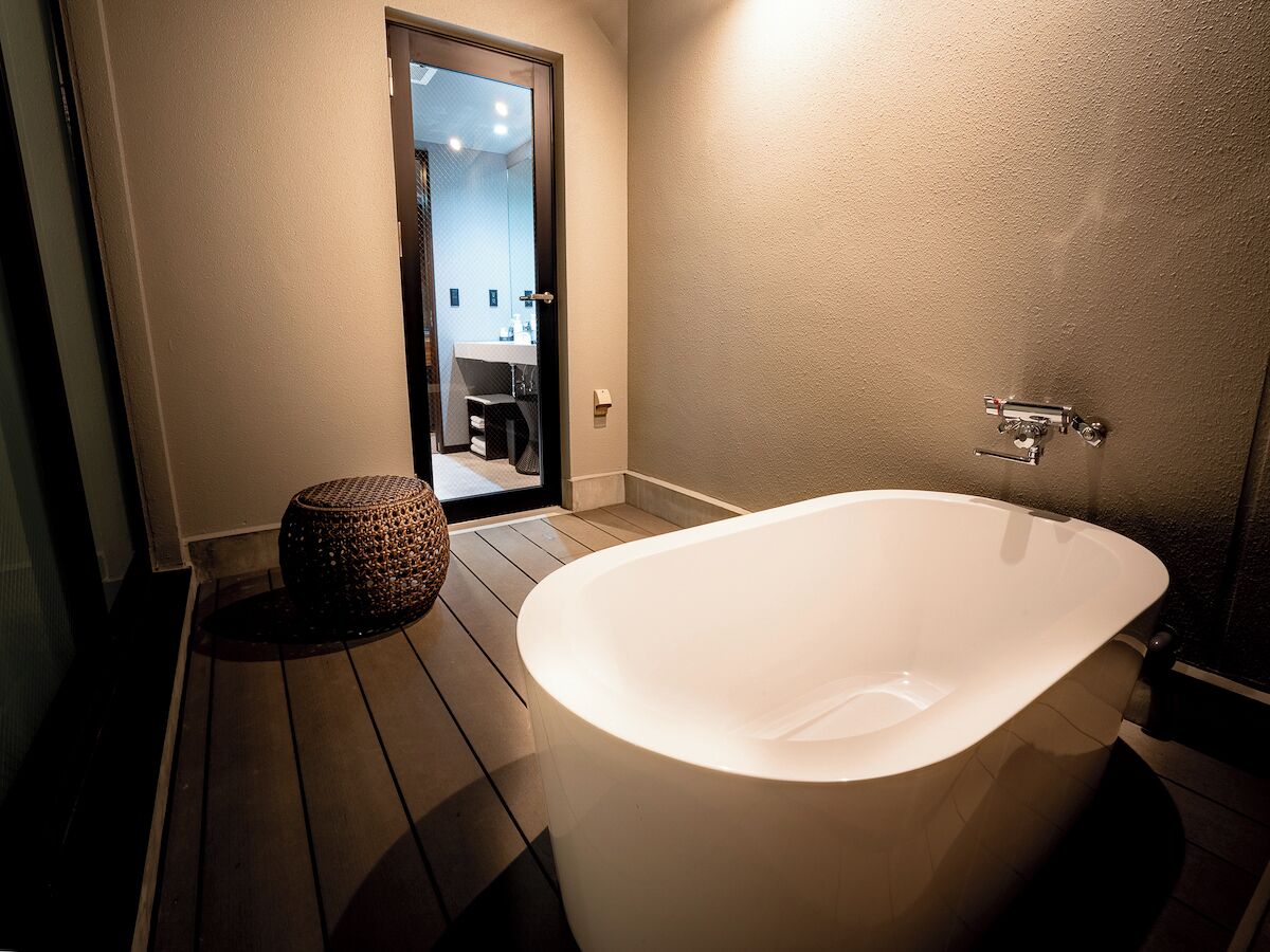 Un baño moderno con una bañera independiente, suelo de madera y un otoman redondito.