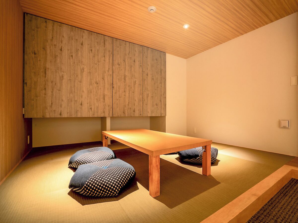 A minimalist room with a wooden ceiling, a low table, and patterned cushions.