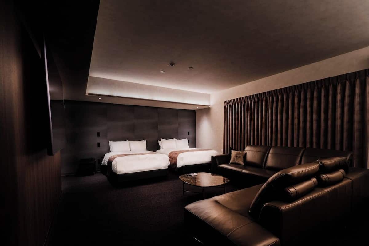 Una habitación de hotel moderna con una cama grande, un sofá, una mesita de centro y un televisor montado en la pared.