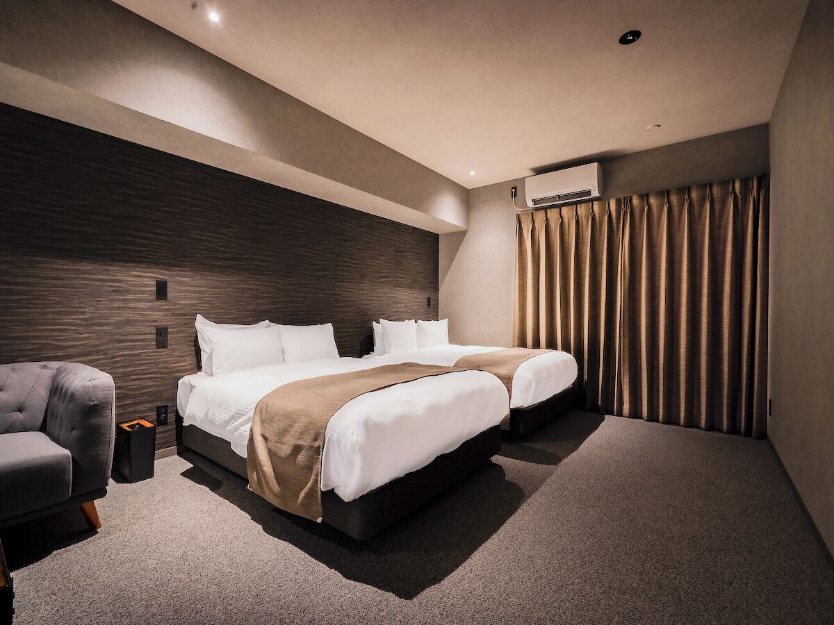 A hotel room with a large bed, a sofa, and an air conditioning unit.