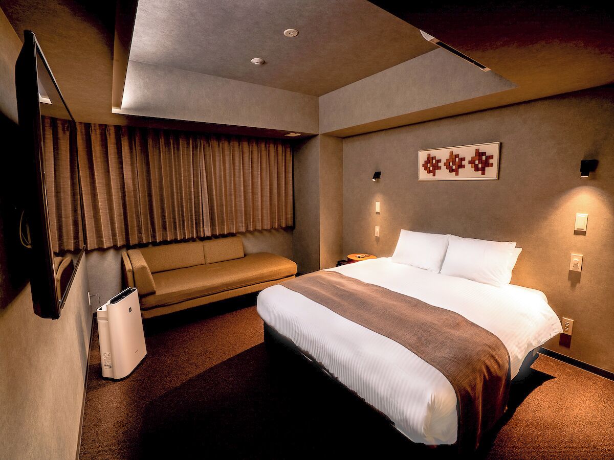 A hotel room with a bed, a sofa, a TV, and a wall-mounted light fixture.