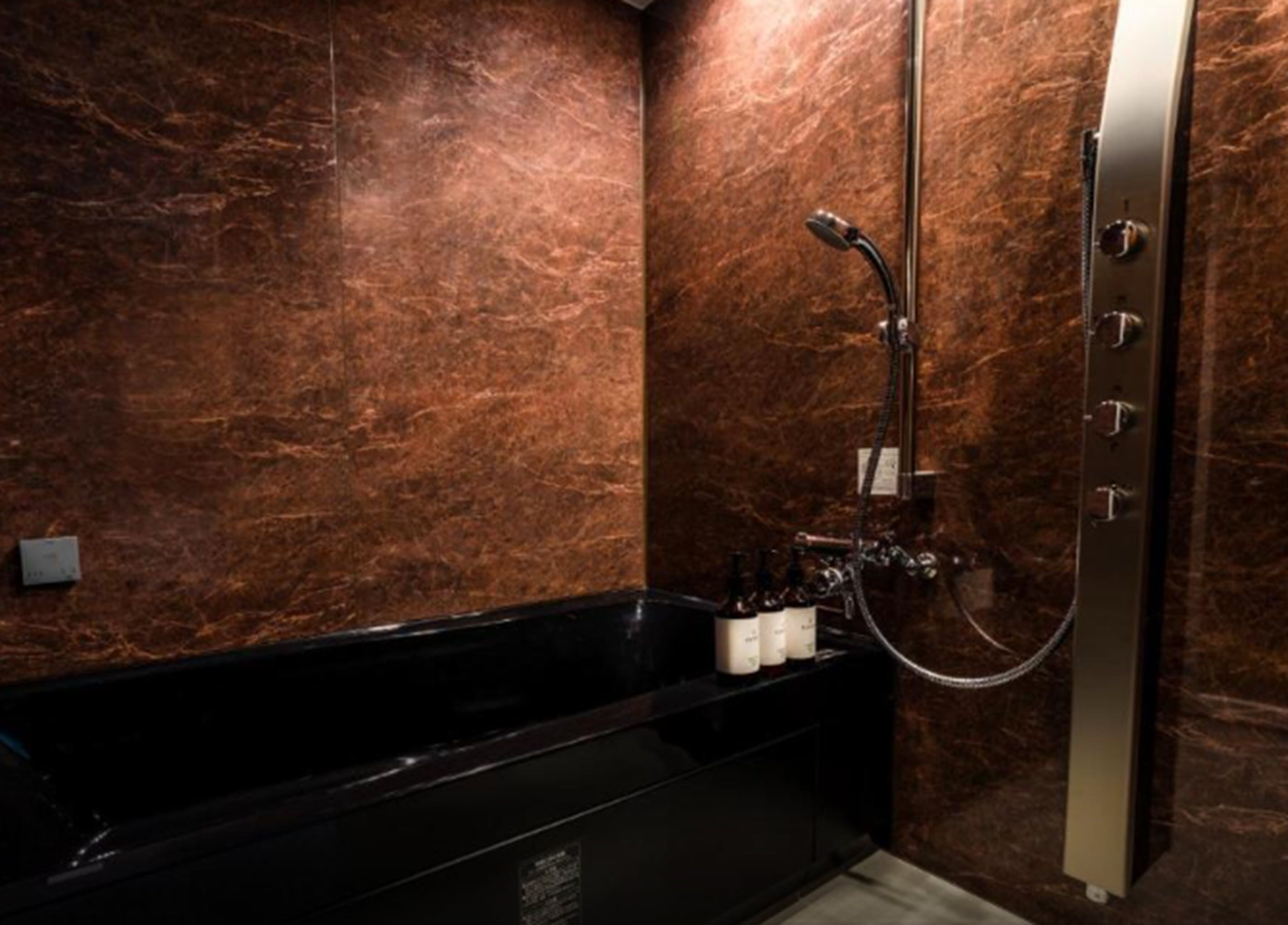 A bathroom with a black bathtub, a shower with a handheld showerhead, and a marble wall.