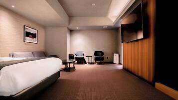 A hotel room with a bed, two chairs, a small table, a TV, and a wooden panel wall.