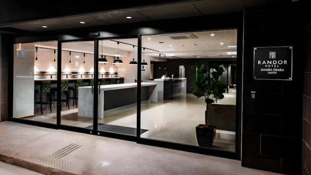 Het uiterlijk van Hotel Randor, met een modern ontwerp, met een glazen entree, een receptie en een bord met de naam en locatie van het hotel.