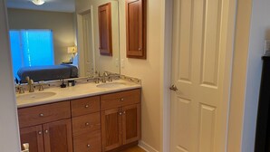A bathroom with a double sink vanity, wooden cabinets, a mirror, and a door. - Ultra Modern Condo located in the Heart of Yachats! Walk to everything! (Yachats)