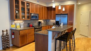 A modern kitchen with wooden cabinets, a stainless steel refrigerator, a microwave, and a granite countertop. - Ultra Modern Condo located in the Heart of Yachats! Walk to everything! (Yachats)