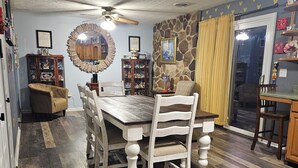 Un comedor con una mesa y sillas de madera, un ventilador de techo y una pared de acento de piedra.