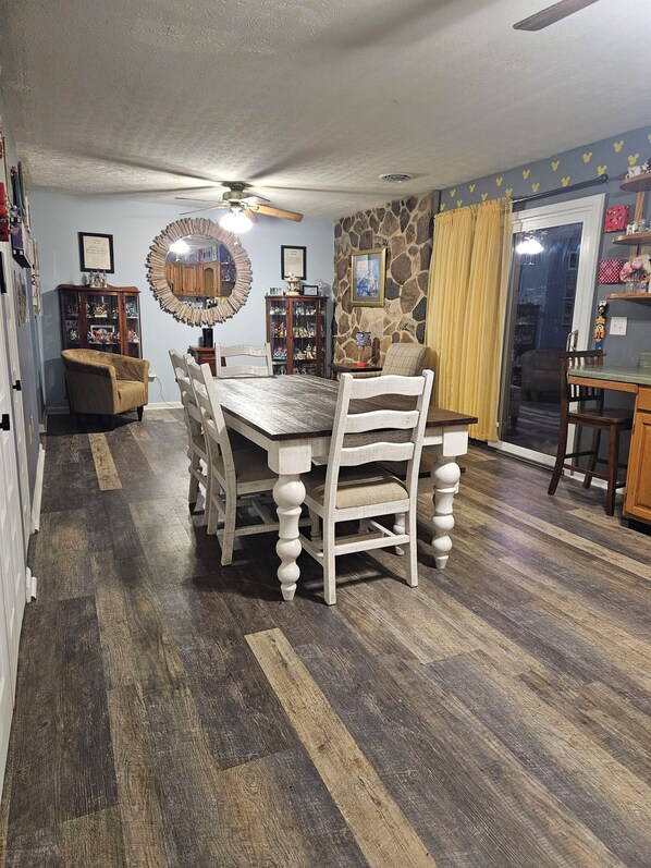 A dining area with a wooden table and chairs, a ceiling fan, and a stone accent wall.