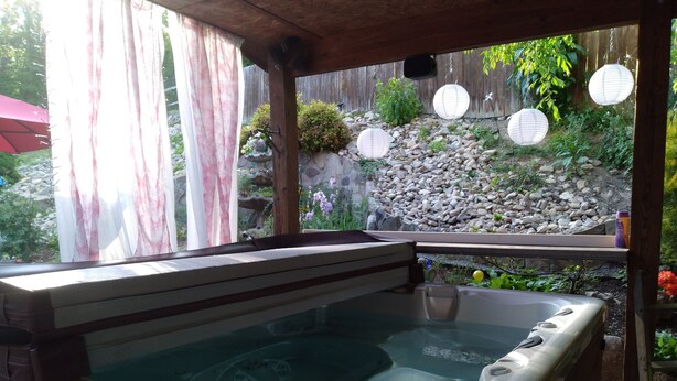 Un jacuzzi en un área exterior cubierta con una terraza de madera, pared de piedra y farolillos de papel colgantes.