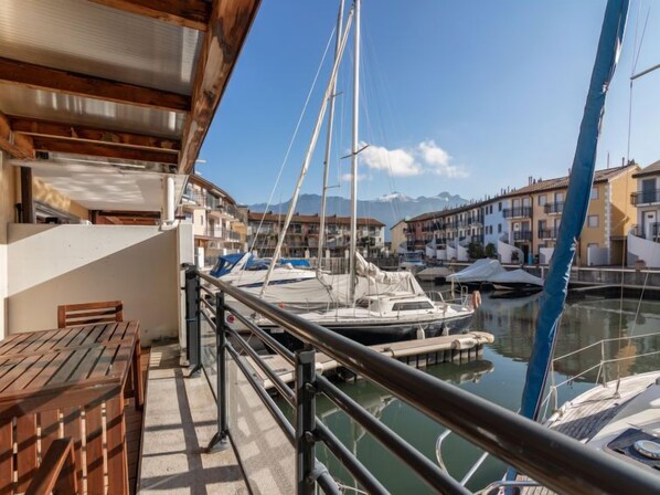 A marina with boats docked, a wooden deck, and buildings in the background.