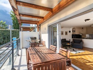 Eine Holzterrasse mit Tisch und Stühlen, eine Schiebetür zu einer Küche und Blick auf einen Berg.
