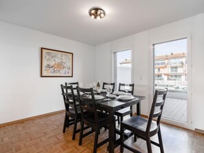 A dining area with a table set for four, chairs, a ceiling light, and a large window with a view of buildings.