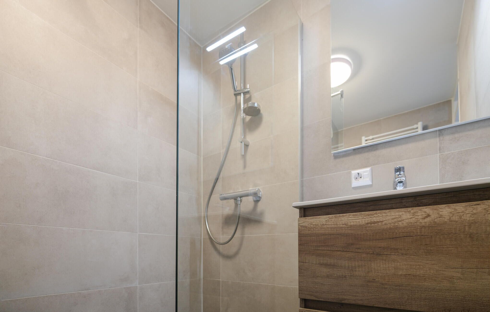 A modern bathroom with a glass shower enclosure, a wooden vanity, and a mirror above the sink.