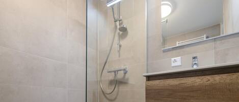 A modern bathroom with a glass shower enclosure, a wooden vanity, and a mirror above the sink.