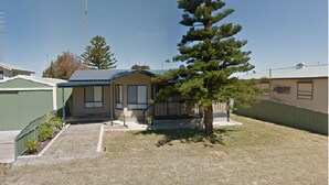 A single-story mobile home with a fenced yard, a small porch, and a tree.