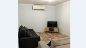 A living room with a black sofa, a beige sofa, a TV on a wooden stand, and an air conditioner on the wall.