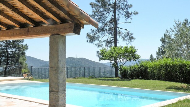 Une piscine surmontée d’une pergola, entourée d’une cour clôturée avec des arbres et, au loin, une montagne.