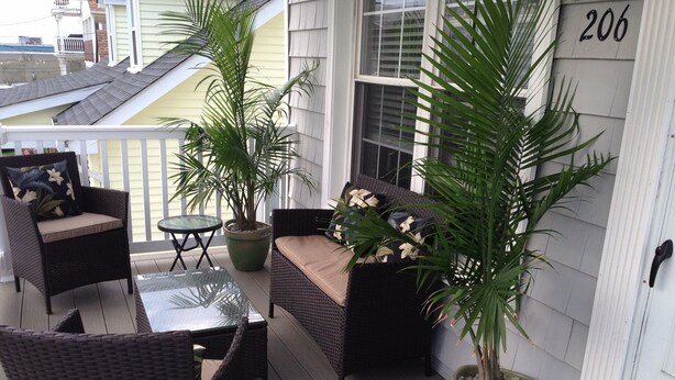 A covered porch with wicker furniture, a glass table, and potted plants.
