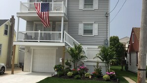 A two-story house with a white garage door, a balcony with an American flag, and a well-maintained front yard with various plants.