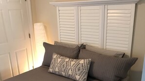 A neatly made bed with a beige bedspread and two pillows, a white door, and a white headboard with horizontal slats.