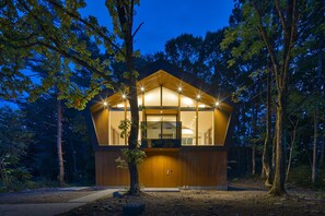 A modern wooden cabin with large windows, surrounded by trees, at dusk. - Ahiru Chalet (Hakuba)