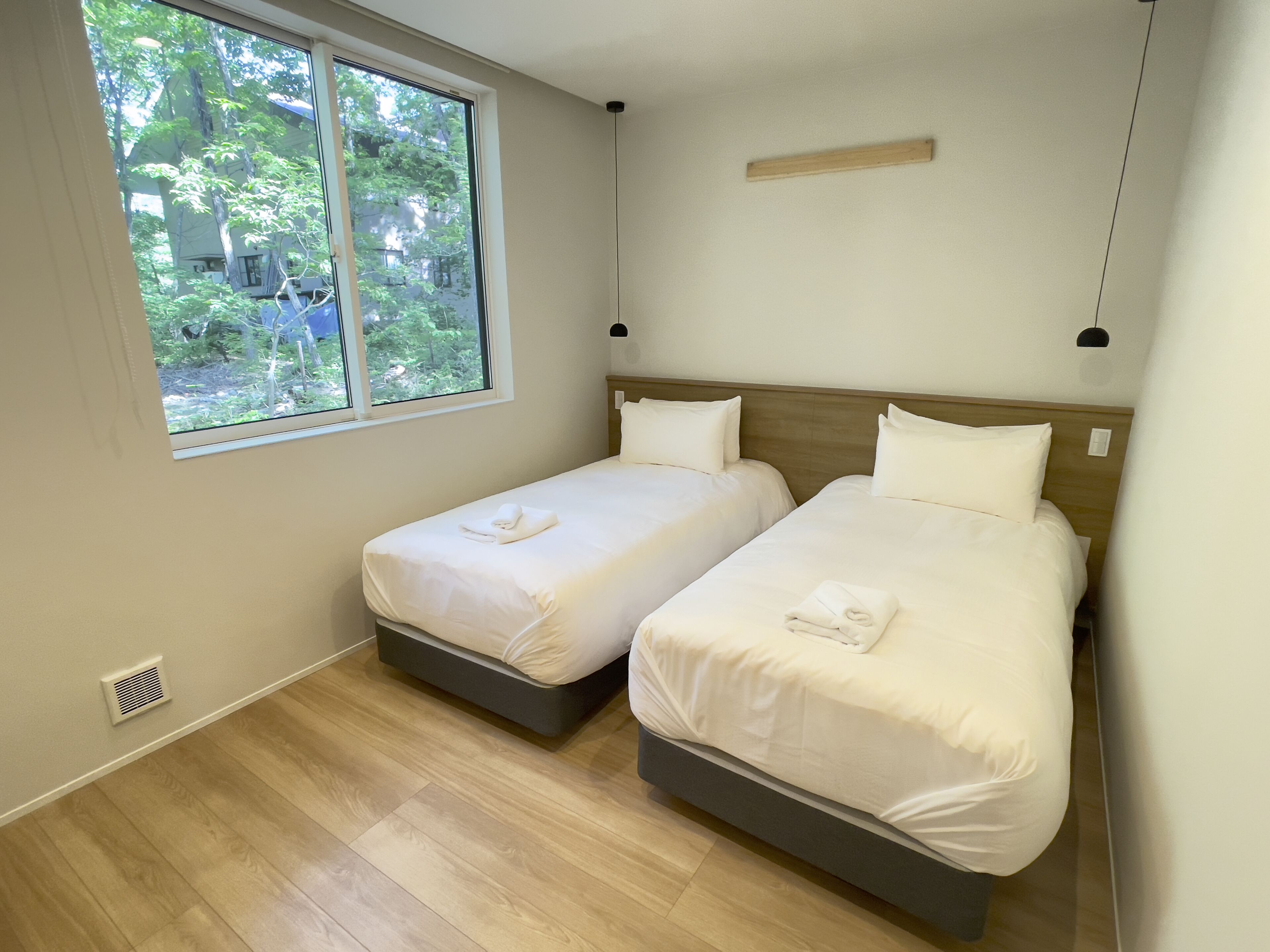 A room with two beds, a window, and a view of greenery outside.