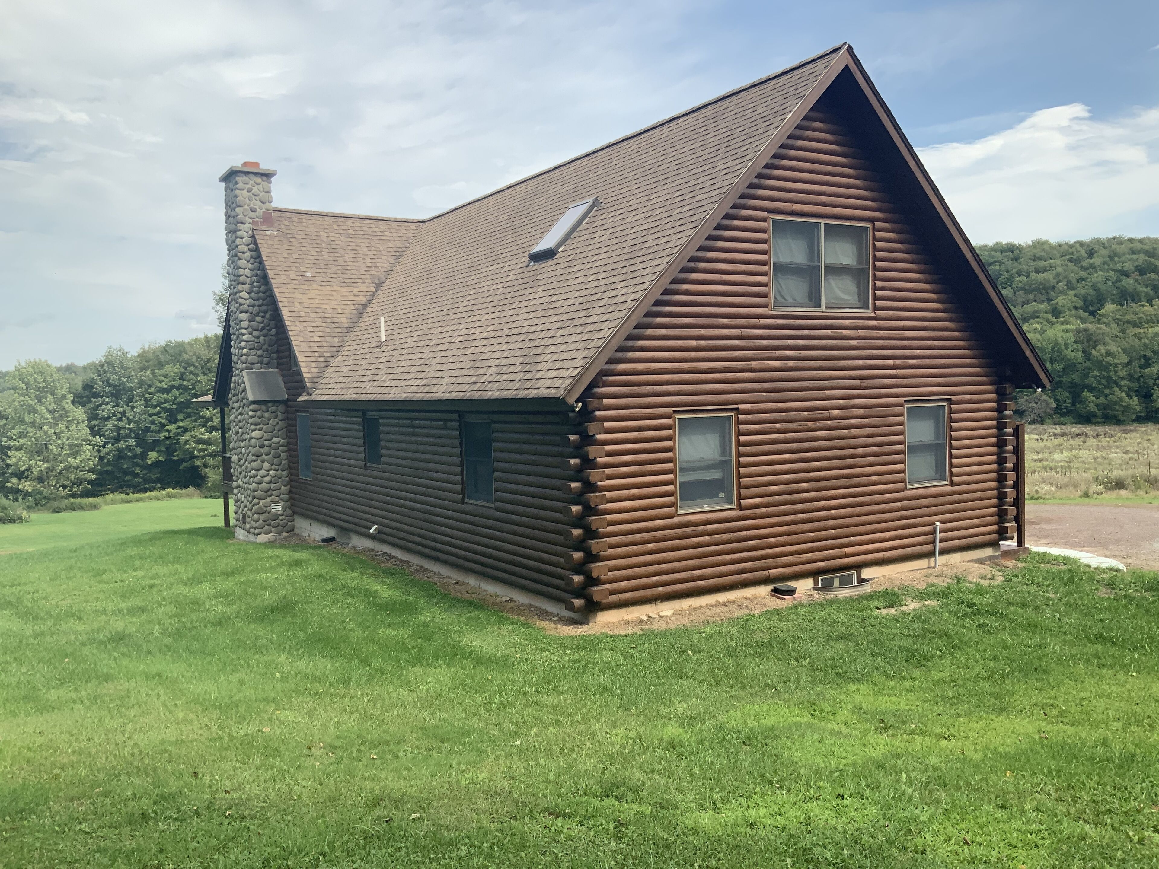 A log cabin with a stone chimney, a sloped roof, and a small porch.