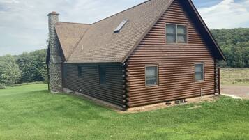 A log cabin with a stone chimney, a sloped roof, and a small porch.