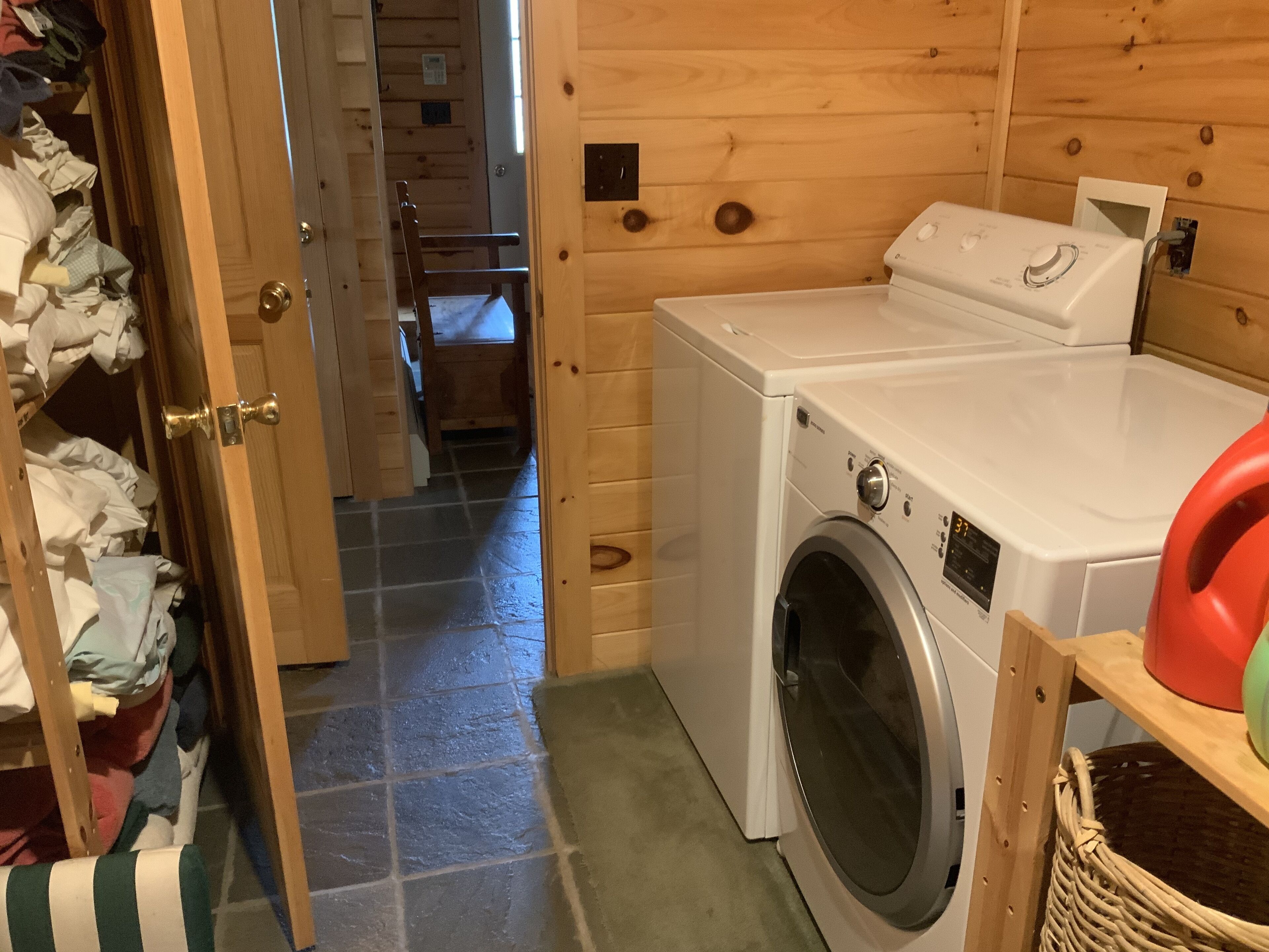 Una lavanderia con lavatrice e asciugatrice, una porta in legno e un cesto su uno scaffale.