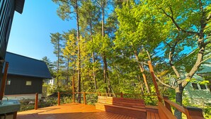 A wooden deck with a metal railing, surrounded by trees and a house. - Cherrywoods Place (Hakuba)