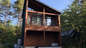 A modern two-story cabin with a wooden exterior, large windows, and a balcony. - Cherrywoods Place (Hakuba)